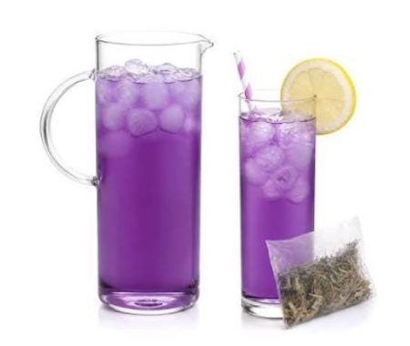 Vibrant purple butterfly pea iced tea in a pitcher and glass with lemon and a striped straw at SereniTea Boutique