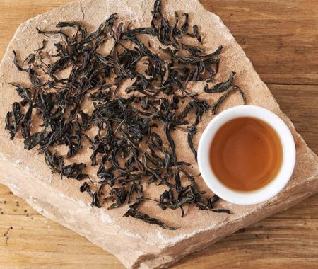 Dark oolong tea leaves spread on a stone slab beside a cup of amber brewed tea at SereniTea Boutique