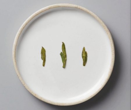 Three delicate green tea leaf buds on a white ceramic plate at SereniTea Boutique
